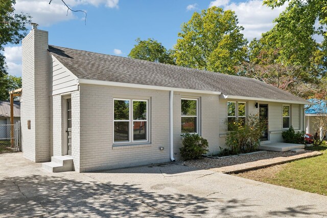 ranch-style house featuring roof with shingles, a chimney, and brick siding