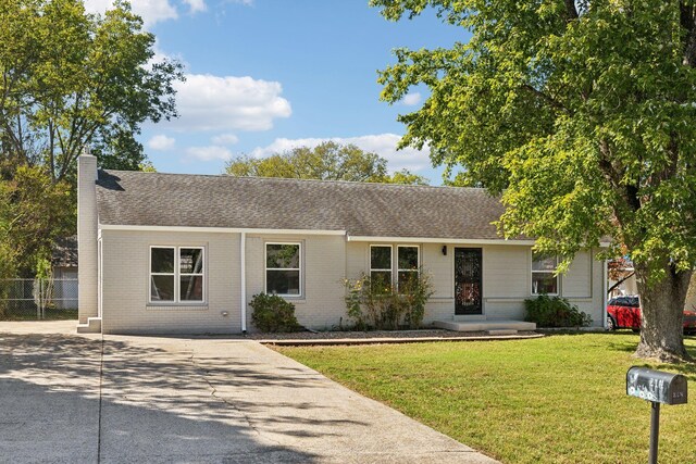 ranch-style house featuring brick siding, concrete driveway, a chimney, roof with shingles, and a front yard