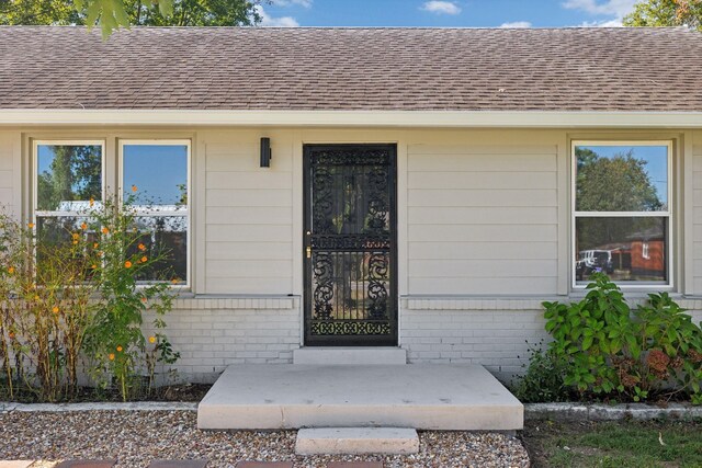 doorway to property with a shingled roof and brick siding