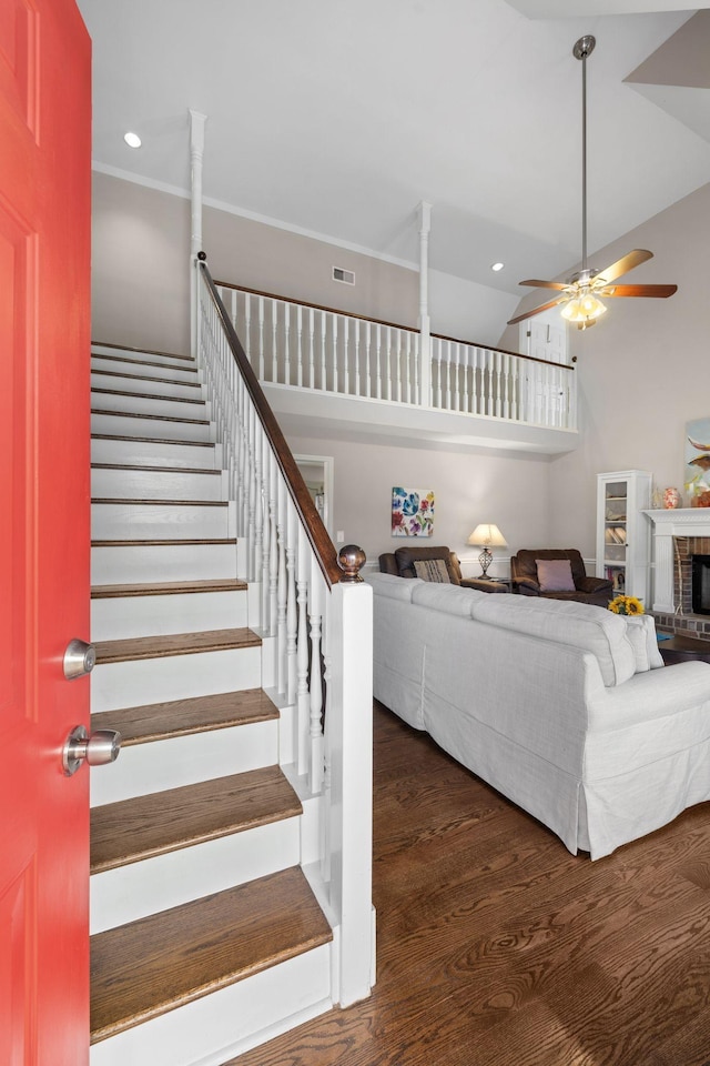 interior space featuring ceiling fan, dark wood-type flooring, visible vents, stairs, and a brick fireplace