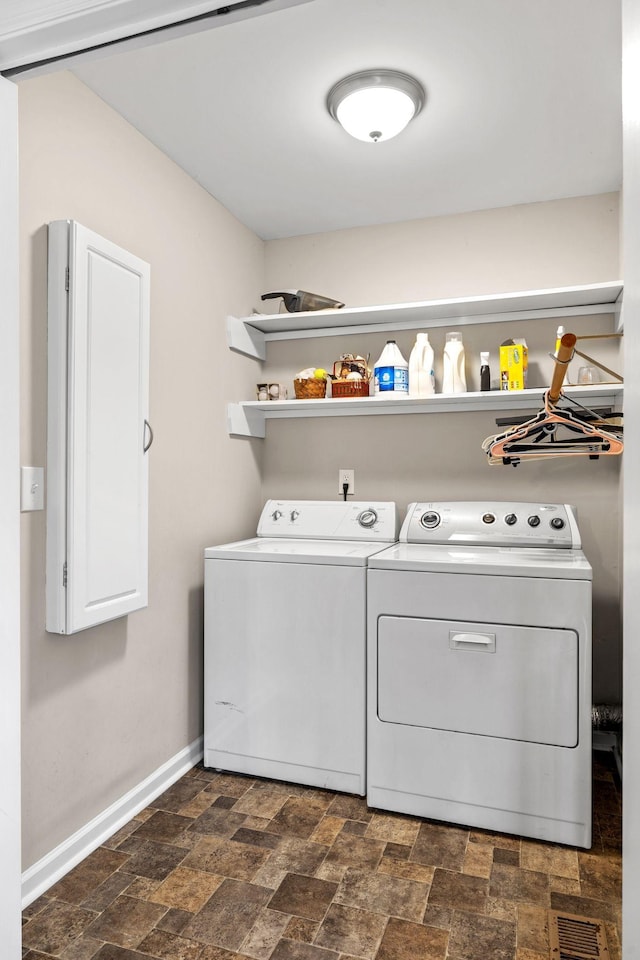 laundry room with washing machine and dryer, stone finish flooring, visible vents, and baseboards