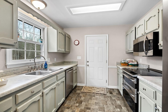 kitchen with stainless steel appliances, light countertops, stone finish flooring, a sink, and baseboards