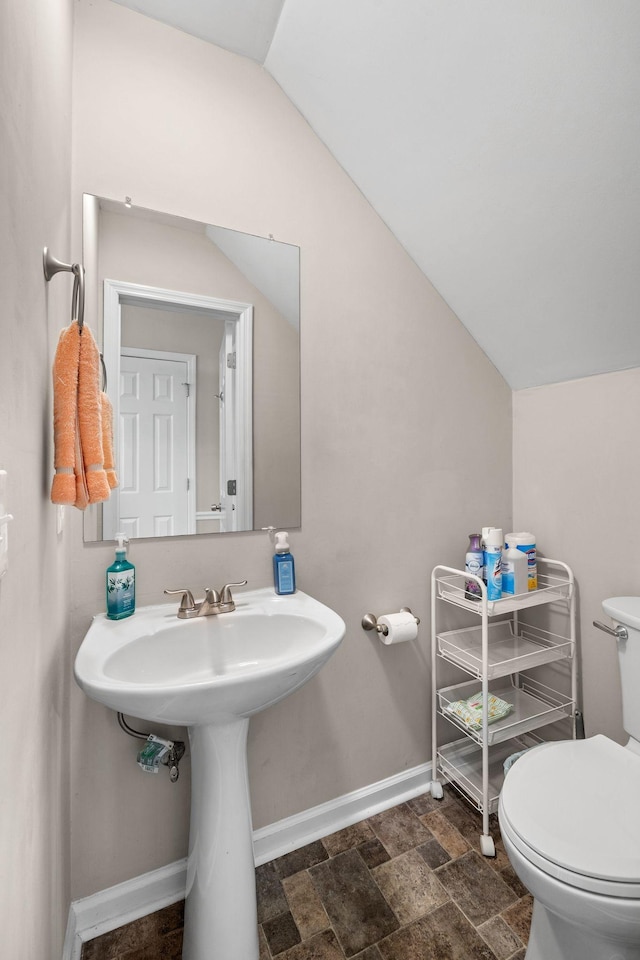 half bath featuring lofted ceiling, stone finish flooring, baseboards, and toilet