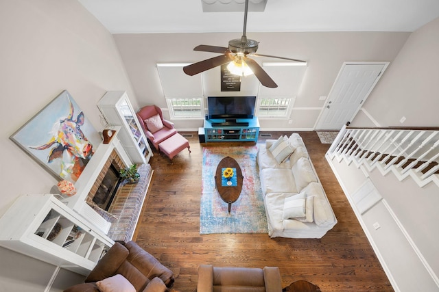 living area with baseboards, ceiling fan, dark wood-type flooring, stairs, and a fireplace