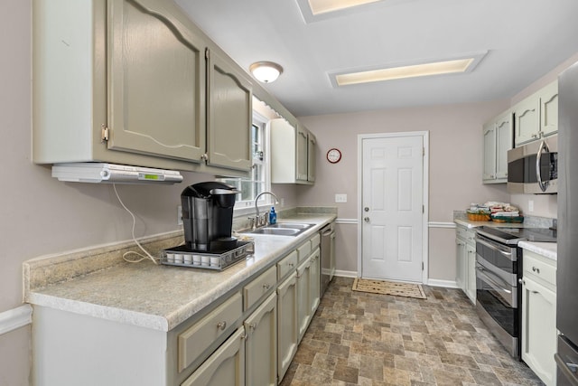 kitchen with baseboards, appliances with stainless steel finishes, stone finish flooring, light countertops, and a sink