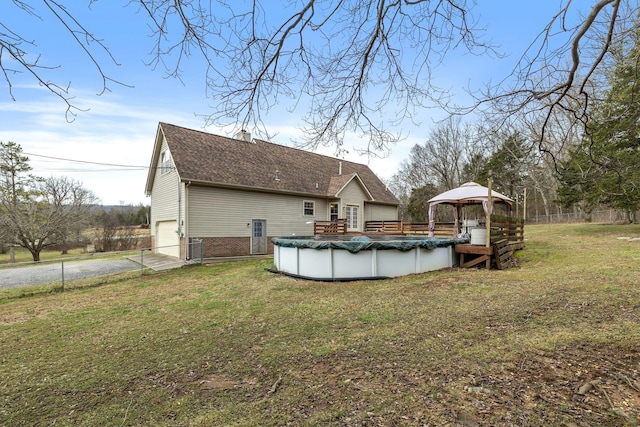 rear view of property featuring a yard, a gazebo, a garage, a covered pool, and driveway