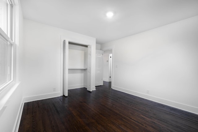 unfurnished bedroom featuring a closet, dark wood-style flooring, and baseboards