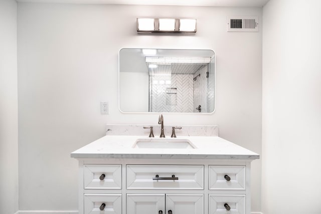 bathroom with visible vents, vanity, and tiled shower