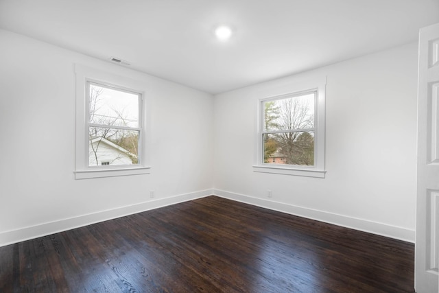 unfurnished room with dark wood-type flooring, a wealth of natural light, visible vents, and baseboards