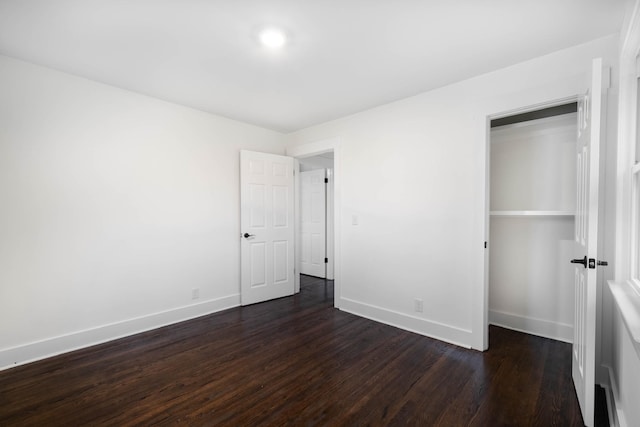 unfurnished bedroom with dark wood-type flooring, a closet, and baseboards