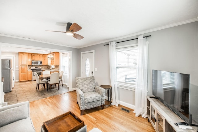 living area with baseboards, light wood-type flooring, visible vents, and crown molding