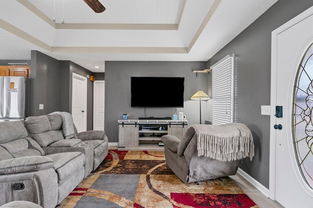 living room featuring a ceiling fan, a raised ceiling, and baseboards