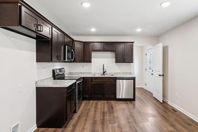 kitchen featuring dark brown cabinetry, stainless steel appliances, a sink, and wood finished floors