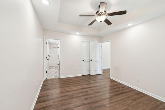 unfurnished bedroom featuring a tray ceiling, dark wood-type flooring, recessed lighting, and baseboards