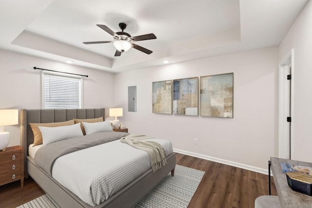 bedroom with a raised ceiling, electric panel, dark wood finished floors, and baseboards