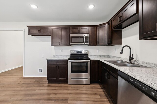 kitchen with appliances with stainless steel finishes, wood finished floors, dark brown cabinets, a sink, and recessed lighting