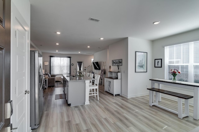 interior space featuring light wood finished floors, open floor plan, a kitchen island with sink, a kitchen breakfast bar, and stainless steel fridge with ice dispenser