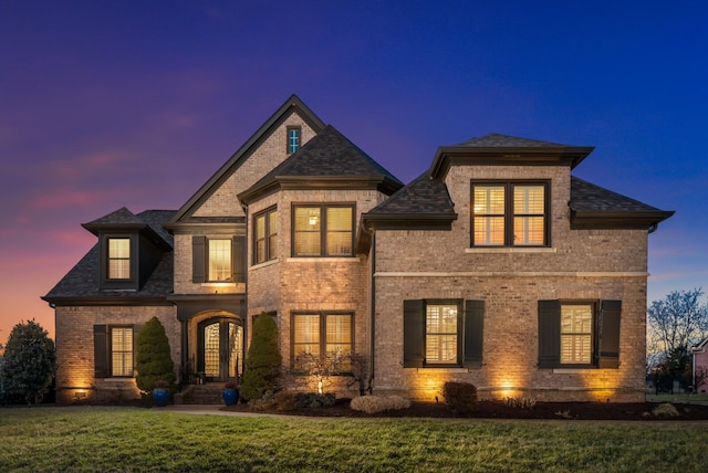 french provincial home featuring french doors, brick siding, and a lawn