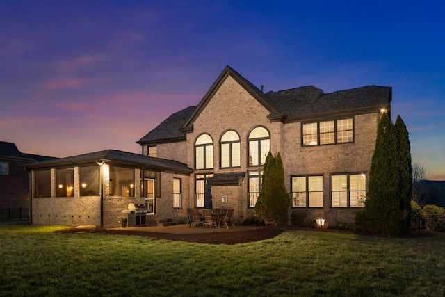 back of house at dusk featuring a patio, a lawn, and brick siding