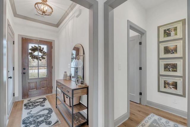 entryway featuring baseboards, a chandelier, light wood-style flooring, and crown molding