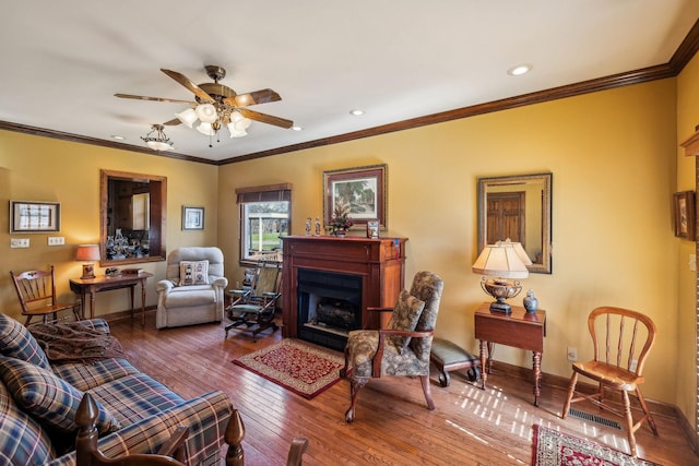 living area featuring ceiling fan, a fireplace, wood finished floors, baseboards, and crown molding