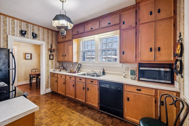 kitchen featuring wallpapered walls, hanging light fixtures, light countertops, black appliances, and a sink