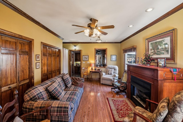 living area with ceiling fan, recessed lighting, wood finished floors, ornamental molding, and a glass covered fireplace