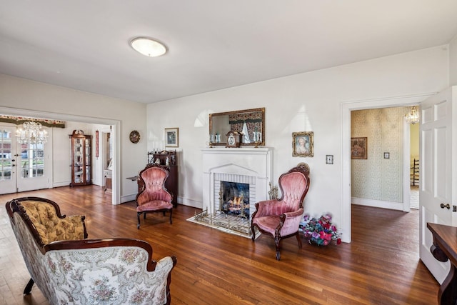 living room with dark wood-style flooring, a brick fireplace, and baseboards