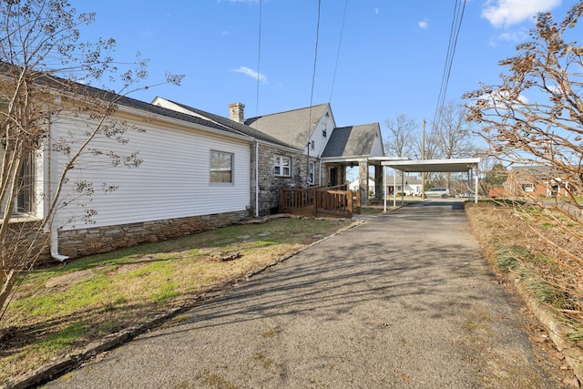 view of side of property featuring driveway, stone siding, and a chimney