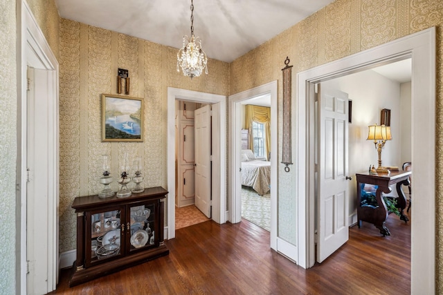 hallway with a chandelier, dark wood finished floors, baseboards, and wallpapered walls