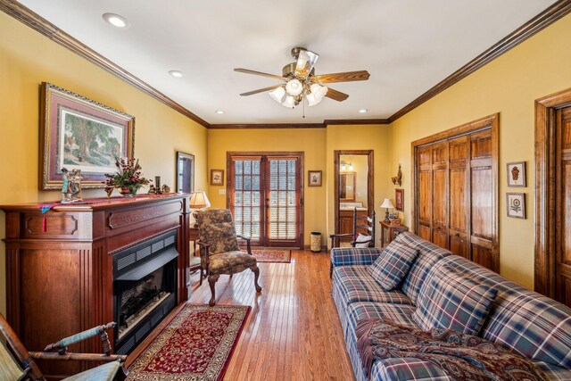 living area featuring light wood-style flooring, a fireplace, crown molding, and french doors