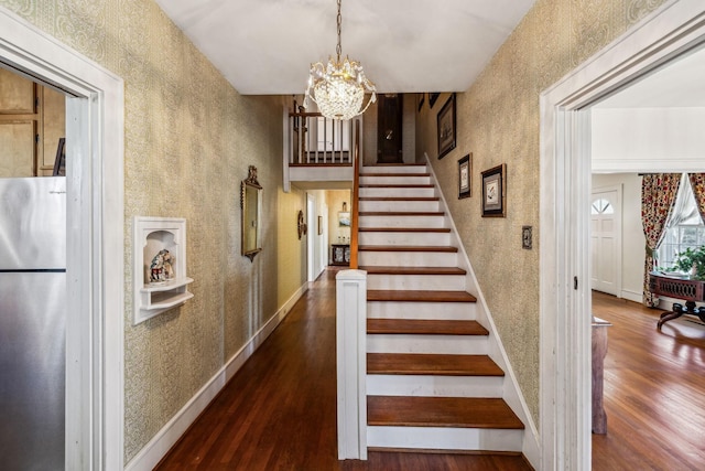 staircase featuring baseboards, a notable chandelier, wood finished floors, and wallpapered walls