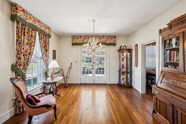 living area with dark wood-style floors, a wealth of natural light, a chandelier, and baseboards