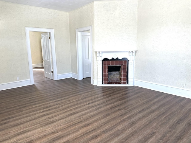 unfurnished living room with dark wood-style floors, a tile fireplace, a textured wall, and baseboards