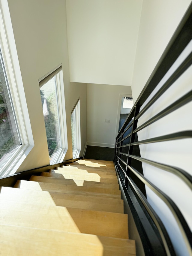 stairway featuring wood finished floors, a towering ceiling, and baseboards