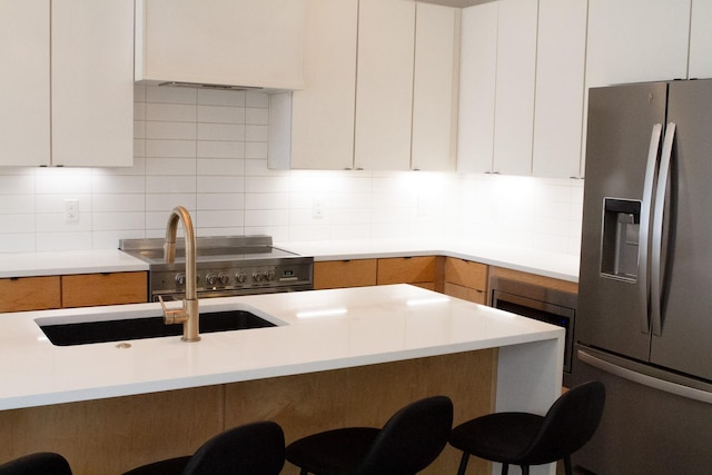 kitchen featuring stainless steel refrigerator with ice dispenser, a breakfast bar area, tasteful backsplash, light countertops, and white cabinetry