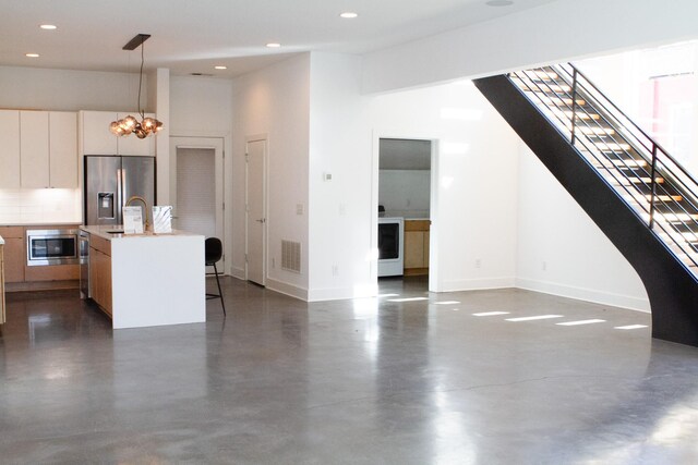 kitchen featuring decorative light fixtures, stainless steel appliances, light countertops, open floor plan, and an island with sink