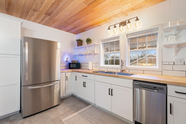 kitchen with wood counters, appliances with stainless steel finishes, a sink, white cabinetry, and backsplash