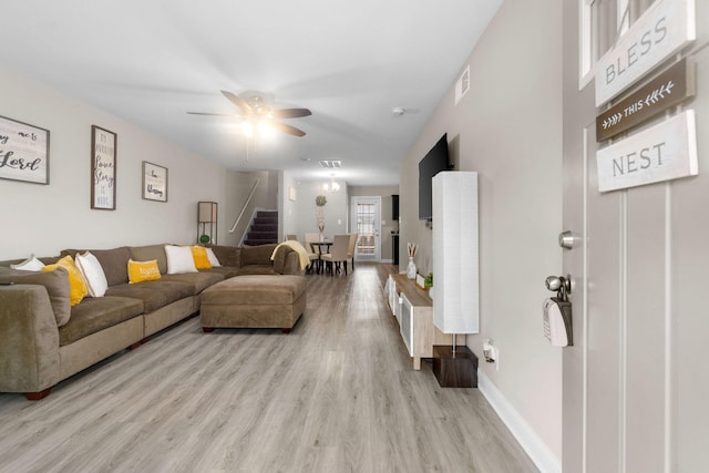 living room with ceiling fan, light wood-style flooring, visible vents, baseboards, and stairway