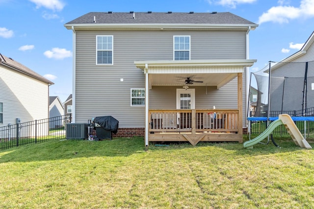 back of house with central AC unit, a trampoline, fence, and a lawn