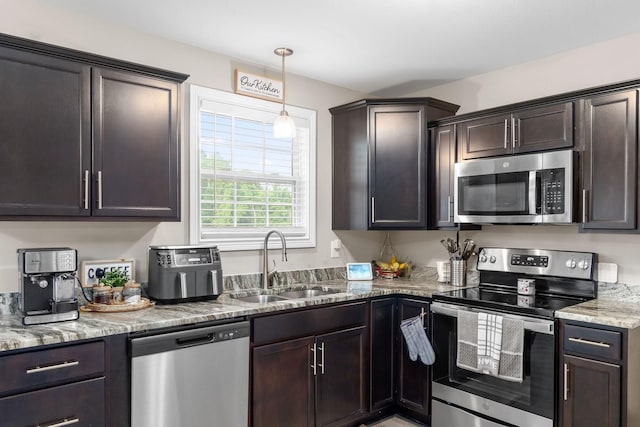 kitchen with stainless steel appliances, a sink, dark brown cabinets, and light stone countertops