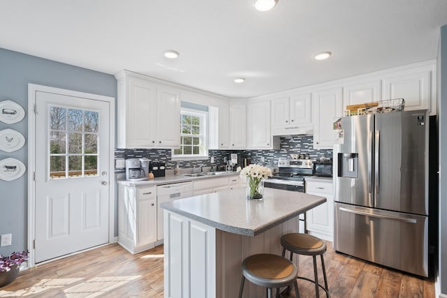 kitchen with under cabinet range hood, a breakfast bar, a kitchen island, white cabinets, and appliances with stainless steel finishes