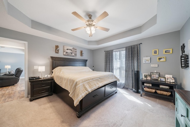 bedroom with a ceiling fan, a raised ceiling, and light carpet