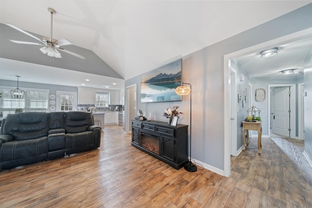 living area with lofted ceiling, ceiling fan with notable chandelier, wood finished floors, and baseboards