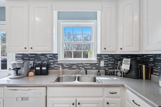 kitchen with white dishwasher, a sink, white cabinetry, light countertops, and backsplash