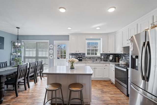 kitchen featuring decorative light fixtures, stainless steel appliances, light countertops, white cabinets, and a kitchen island