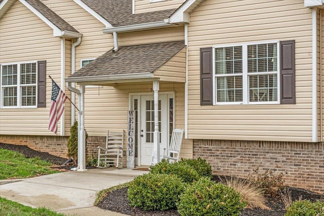 entrance to property with a shingled roof and brick siding