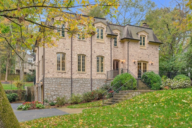 view of front of home with mansard roof, stairway, fence, a front lawn, and brick siding