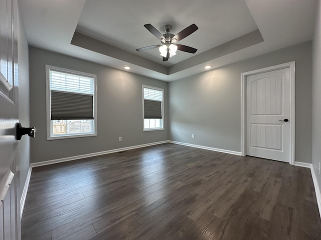 empty room featuring a raised ceiling, dark wood finished floors, and baseboards