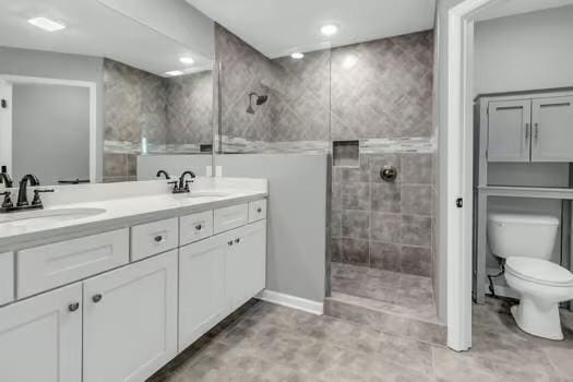 bathroom with toilet, double vanity, walk in shower, and a sink